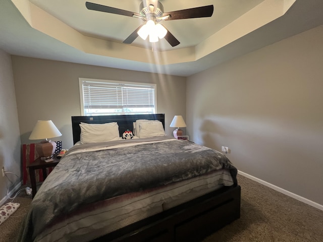 carpeted bedroom with ceiling fan and a tray ceiling