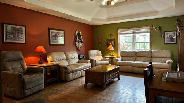 living room featuring ceiling fan, a tray ceiling, and dark hardwood / wood-style flooring