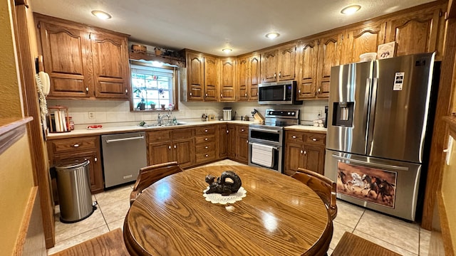 kitchen with appliances with stainless steel finishes, tasteful backsplash, sink, and light tile patterned flooring