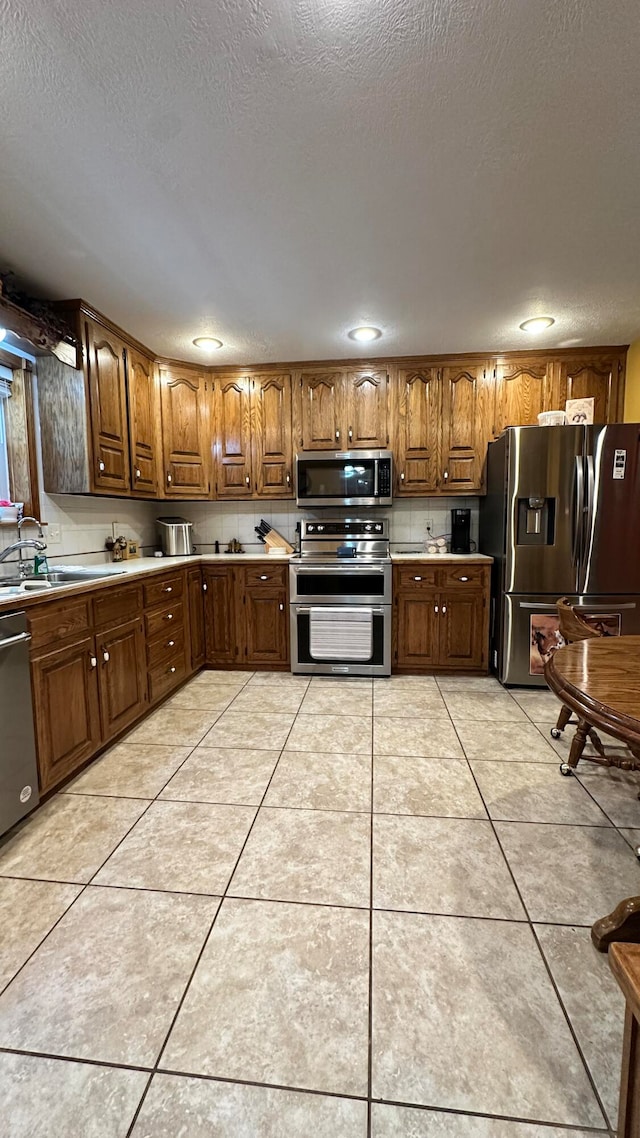 kitchen with appliances with stainless steel finishes, sink, light tile patterned flooring, and a textured ceiling