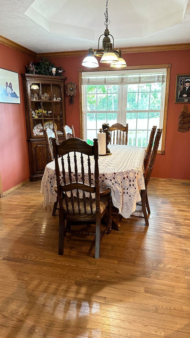 dining area featuring light wood-type flooring, crown molding, a raised ceiling, a notable chandelier, and a textured ceiling