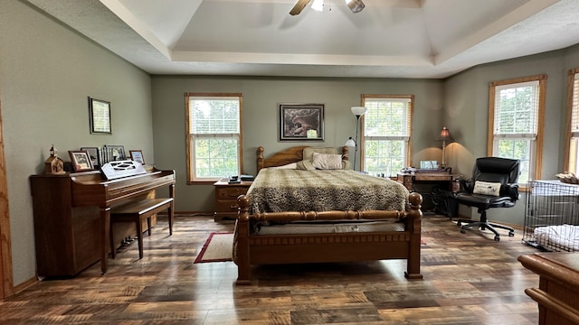 bedroom with ceiling fan, a raised ceiling, dark wood-type flooring, and multiple windows