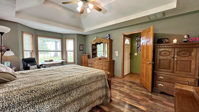 bedroom with ceiling fan, dark wood-type flooring, and a tray ceiling