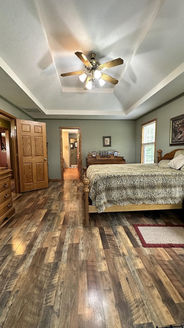 bedroom with a textured ceiling, ceiling fan, a tray ceiling, and dark hardwood / wood-style flooring