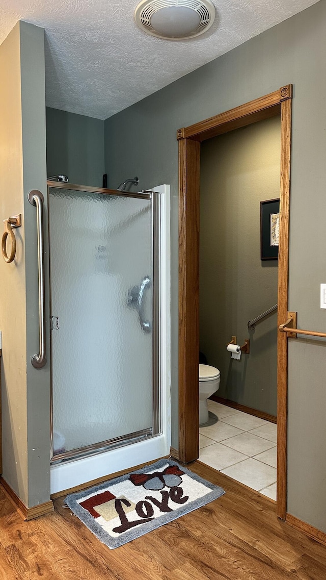 bathroom featuring a shower with door, toilet, wood-type flooring, and a textured ceiling