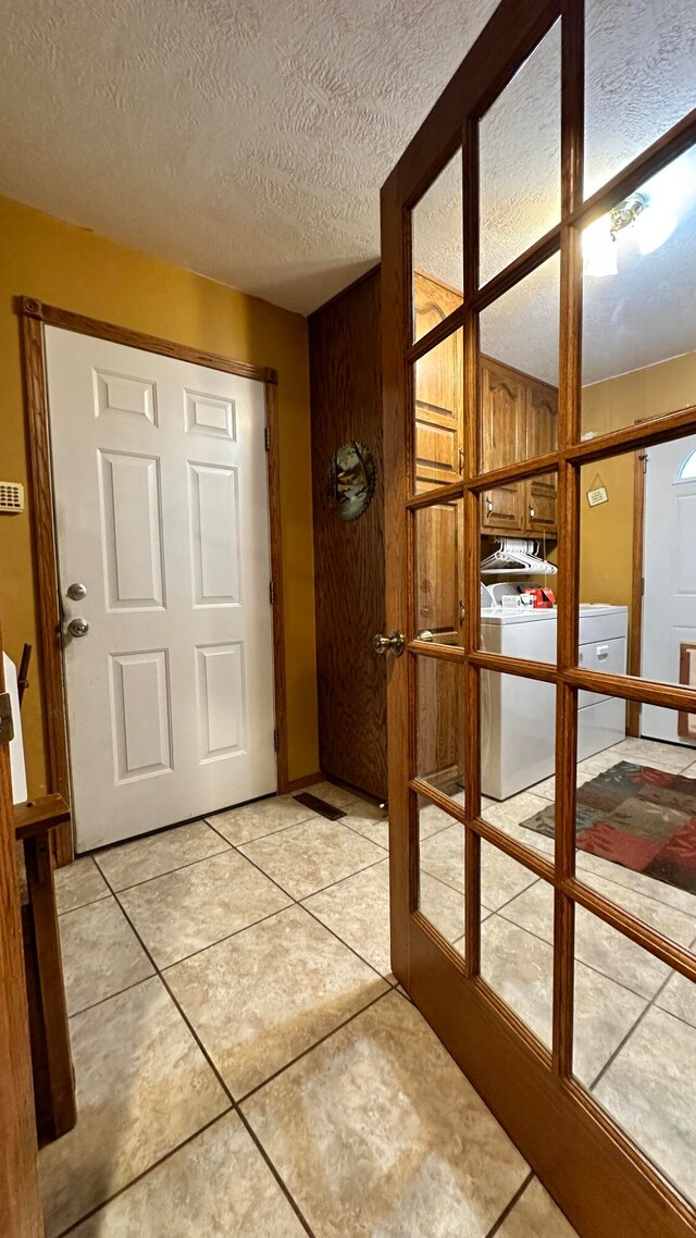 hall featuring light tile patterned flooring, washer and clothes dryer, french doors, and a textured ceiling