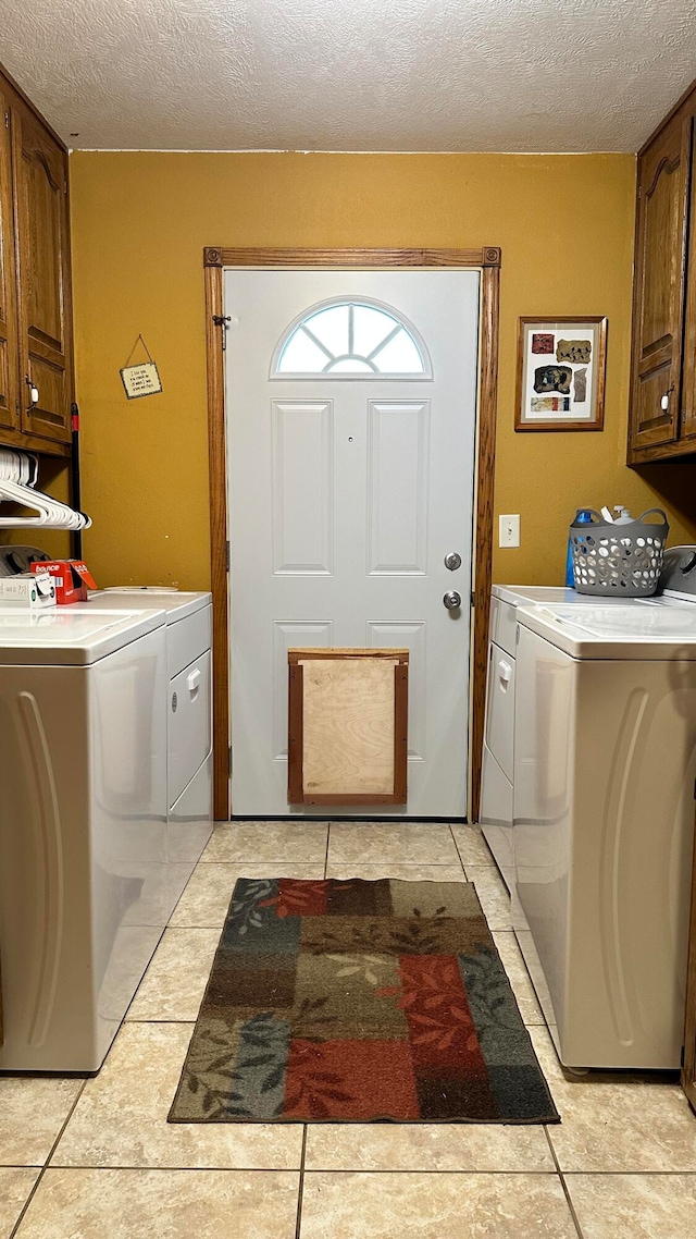 laundry area with a textured ceiling, washer and clothes dryer, light tile patterned floors, and cabinets