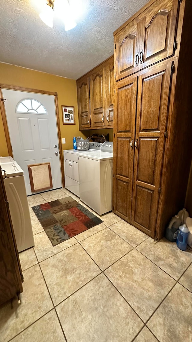 washroom featuring washing machine and clothes dryer, cabinets, light tile patterned floors, and a textured ceiling