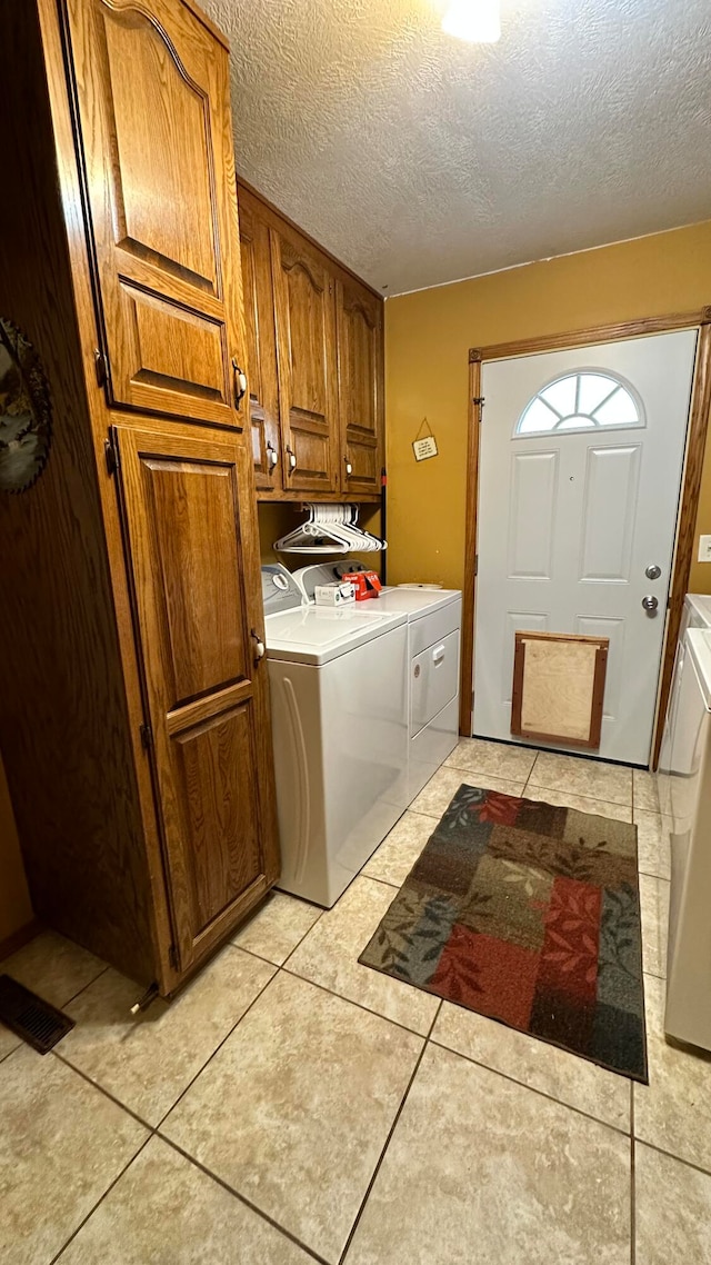 clothes washing area with a textured ceiling, washer and clothes dryer, light tile patterned floors, and cabinets