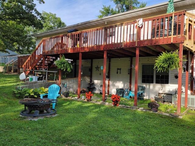 rear view of house with an outdoor fire pit, a lawn, and a deck