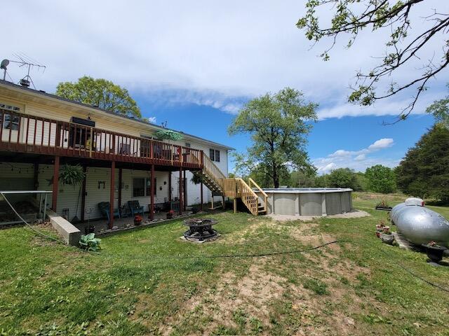 back of property with a lawn, an outdoor pool, a fire pit, a wooden deck, and stairs