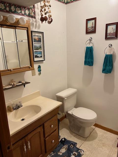 half bath with baseboards, vanity, and toilet
