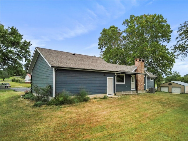 view of front of house with a garage, central air condition unit, a front lawn, and an outbuilding