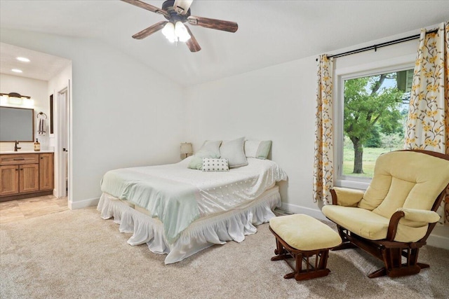 bedroom featuring ceiling fan, light colored carpet, vaulted ceiling, sink, and ensuite bath