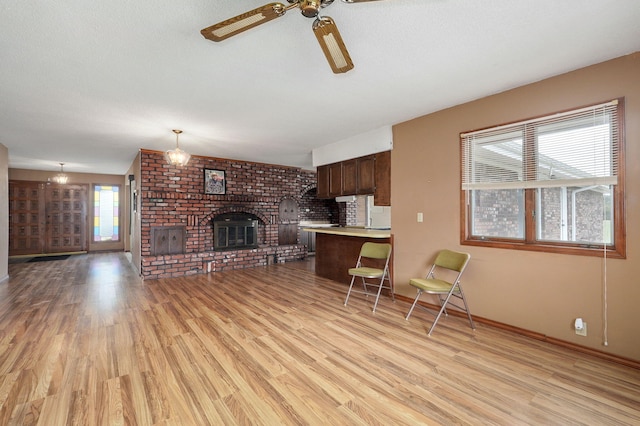 living room with a brick fireplace, ceiling fan, light hardwood / wood-style floors, and a textured ceiling