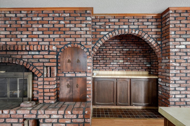 interior space with a brick fireplace, dark brown cabinets, brick wall, and a textured ceiling