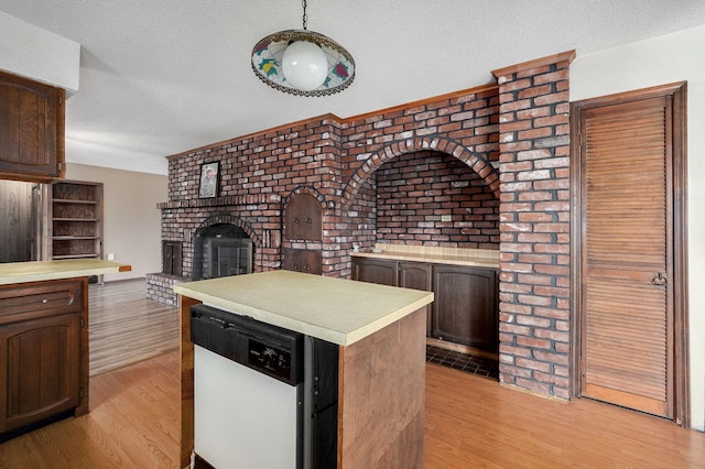 kitchen featuring a brick fireplace, dishwasher, light hardwood / wood-style flooring, and a textured ceiling