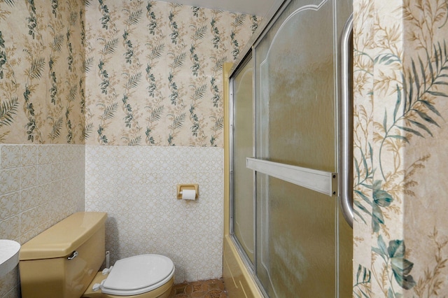 bathroom with combined bath / shower with glass door, tile walls, and toilet