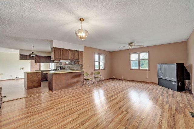 kitchen with pendant lighting, kitchen peninsula, tasteful backsplash, ceiling fan with notable chandelier, and light hardwood / wood-style floors