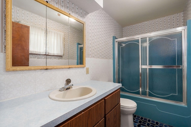 full bathroom featuring bath / shower combo with glass door, vanity, tile walls, and toilet