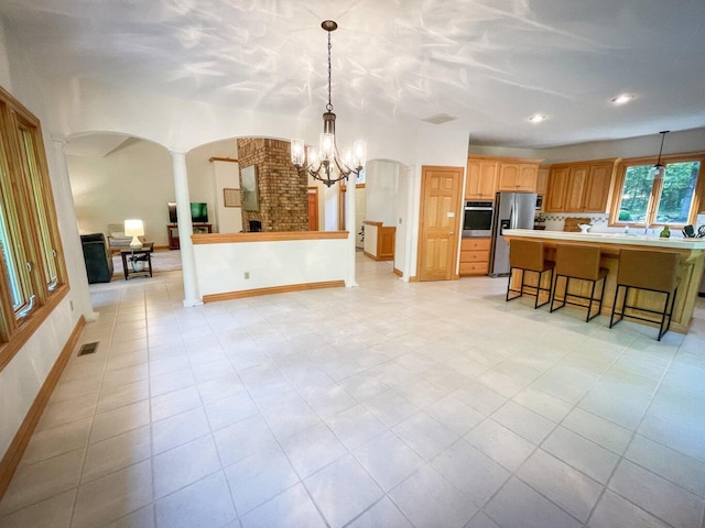 kitchen featuring a center island, decorative light fixtures, stainless steel appliances, decorative columns, and a breakfast bar area