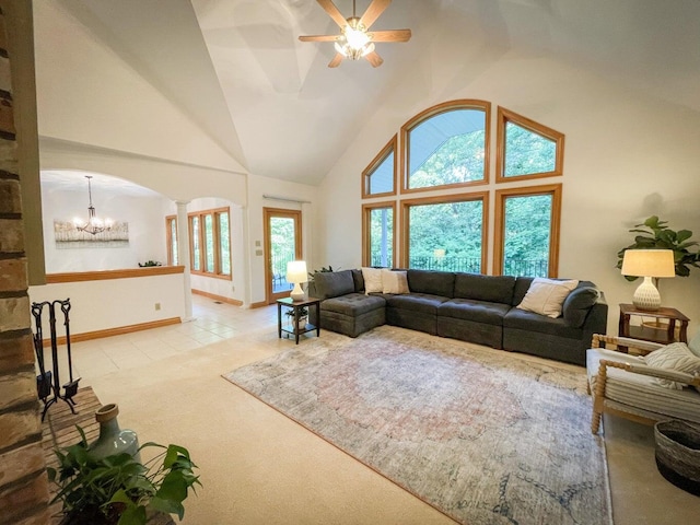 carpeted living room featuring decorative columns, ceiling fan with notable chandelier, and high vaulted ceiling