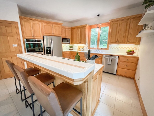 kitchen featuring a center island, tile counters, stainless steel appliances, hanging light fixtures, and a breakfast bar area