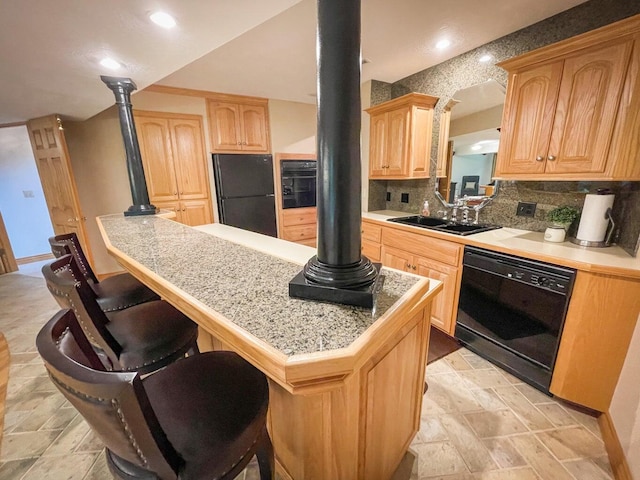 kitchen with black appliances, a kitchen bar, light brown cabinetry, sink, and kitchen peninsula