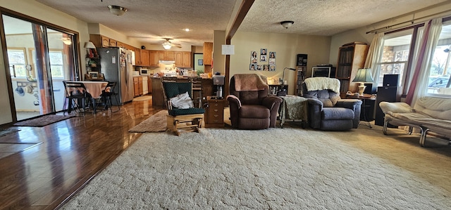 living room with a healthy amount of sunlight, a textured ceiling, ceiling fan, and dark wood-type flooring