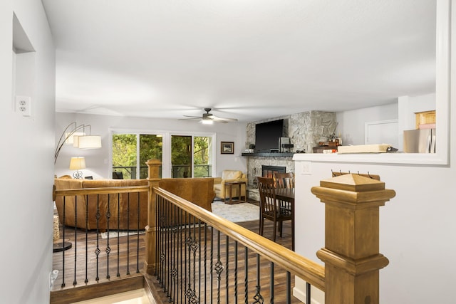 interior space with a stone fireplace, wood finished floors, and a ceiling fan