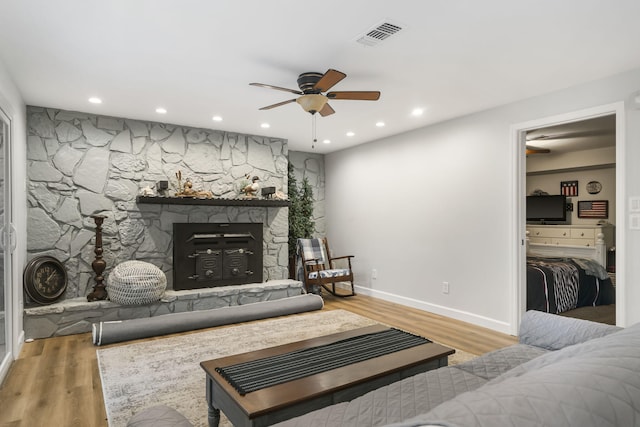 living room featuring hardwood / wood-style flooring, ceiling fan, and a stone fireplace