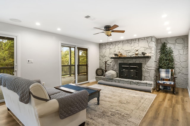 living room featuring hardwood / wood-style flooring, a stone fireplace, and ceiling fan