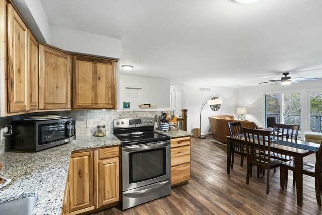 kitchen with appliances with stainless steel finishes, tasteful backsplash, a wood stove, dark hardwood / wood-style flooring, and light stone countertops