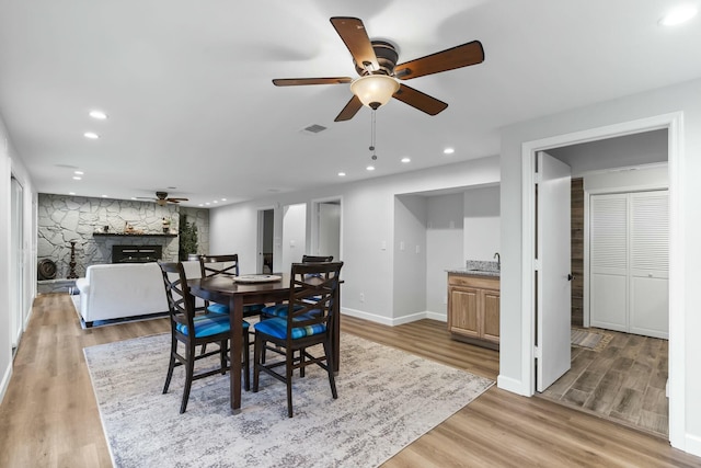 dining space featuring a stone fireplace, hardwood / wood-style floors, and ceiling fan