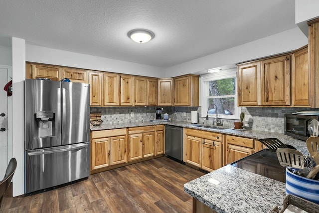 kitchen featuring a sink, backsplash, light stone countertops, stainless steel appliances, and dark wood-style flooring