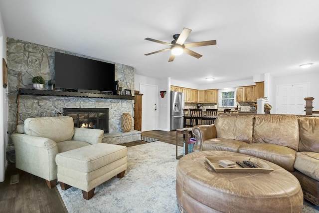 living room featuring hardwood / wood-style flooring, ceiling fan, and a stone fireplace