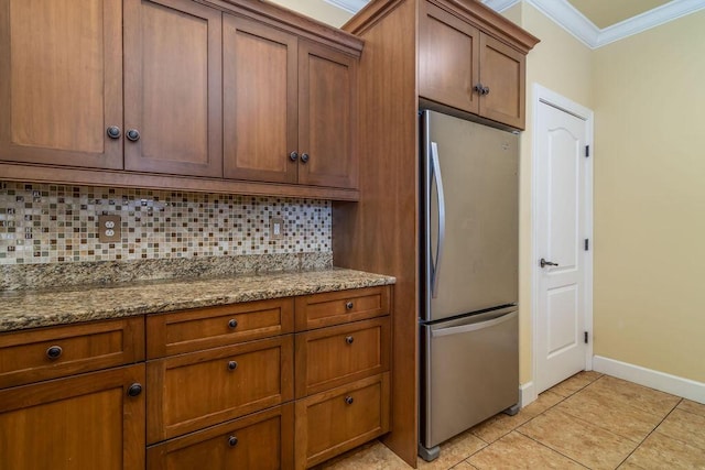 kitchen with tasteful backsplash, light tile patterned floors, ornamental molding, stainless steel fridge, and stone counters