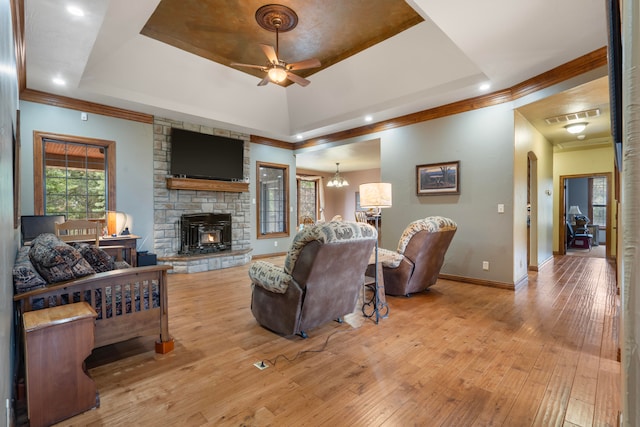 living room featuring ornamental molding, a wood stove, light hardwood / wood-style flooring, a tray ceiling, and ceiling fan with notable chandelier