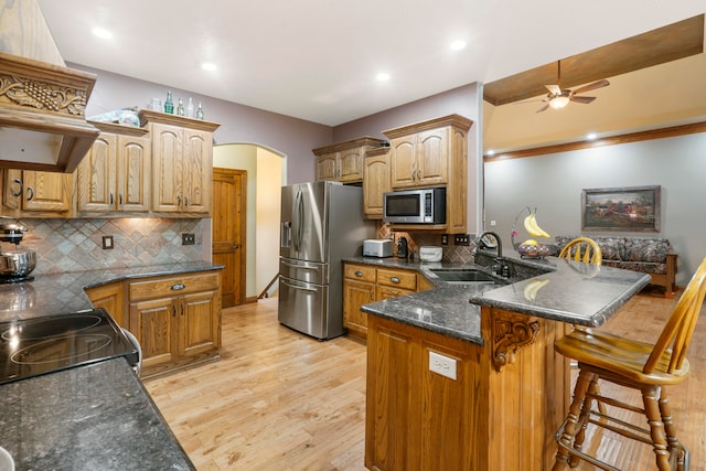 kitchen with sink, light hardwood / wood-style floors, kitchen peninsula, appliances with stainless steel finishes, and a kitchen breakfast bar