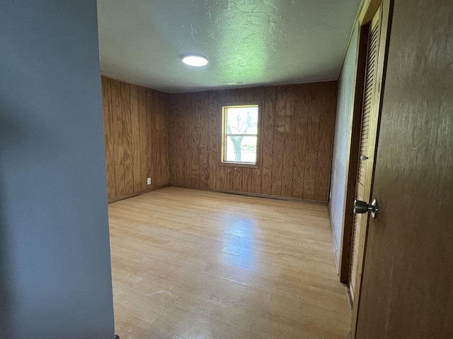 spare room with wood walls, light hardwood / wood-style floors, and a textured ceiling