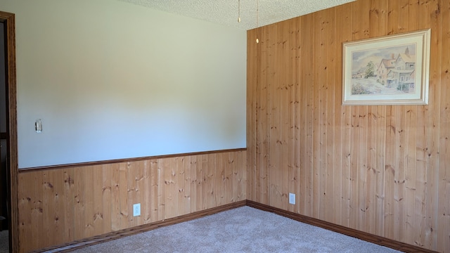 carpeted empty room with wooden walls and a textured ceiling