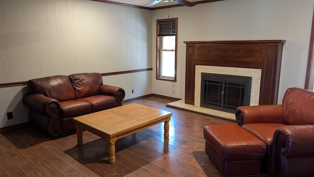 living area featuring a fireplace with raised hearth, dark wood-style flooring, baseboards, and ceiling fan
