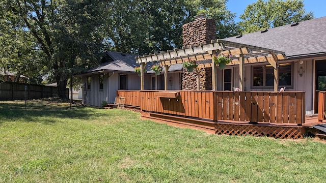 rear view of house with a chimney, a lawn, a deck, a shingled roof, and fence