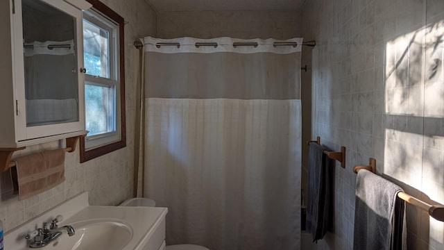 bathroom with walk in shower, vanity, toilet, and tile walls