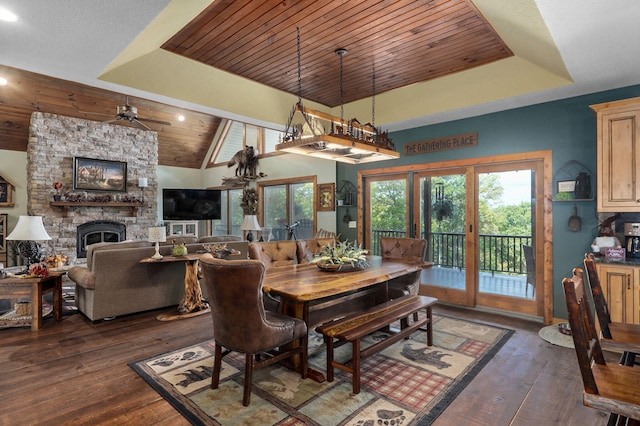 dining room featuring ceiling fan, a stone fireplace, wooden ceiling, dark hardwood / wood-style flooring, and vaulted ceiling