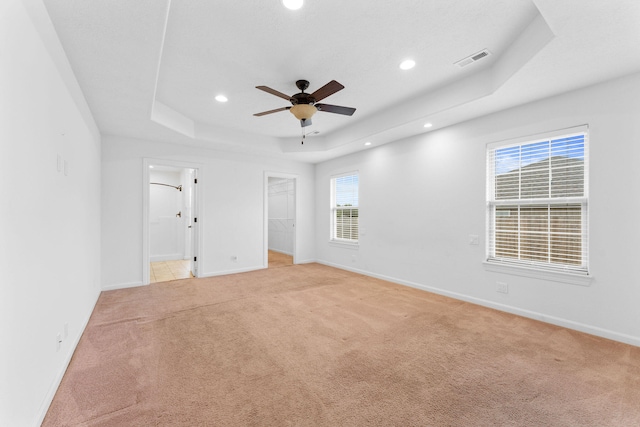 unfurnished room featuring a raised ceiling, light colored carpet, and ceiling fan