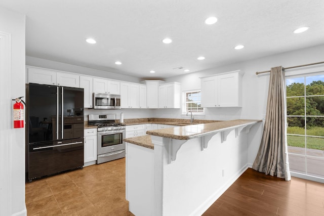 kitchen featuring a breakfast bar, sink, kitchen peninsula, appliances with stainless steel finishes, and white cabinetry