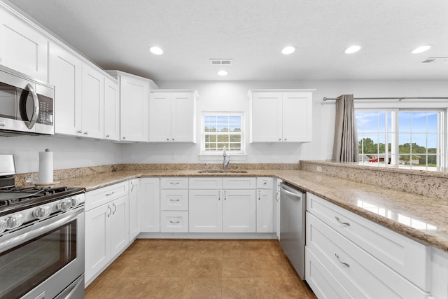 kitchen with light stone counters, white cabinets, appliances with stainless steel finishes, and sink