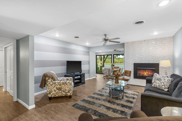 living room featuring a stone fireplace, dark hardwood / wood-style floors, and ceiling fan