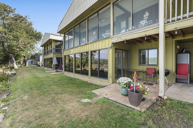 back of property featuring a patio, a lawn, and a sunroom